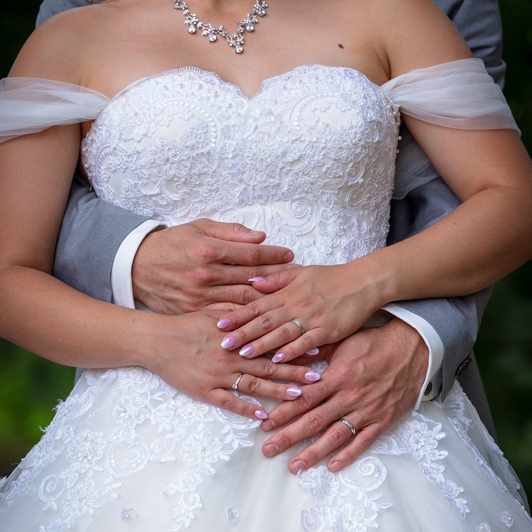 Détail des mains des mariés sur la robe de mariée